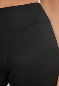 Leggings neri a vita alta realizzati in tessuto elasticizzato, dotati di cuciture piatte e una texture liscia. Nessun marchio o motivo visibile.