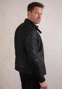 Black leather jacket with a structured design, snap collar, and visible stitching. Features a smooth texture and fitted silhouette.