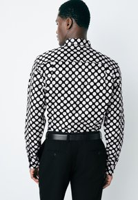 Camicia a maniche lunghe nera con motivo a pois bianchi, caratterizzata da colletto e stile con bottoni, abbinata a pantaloni neri e cintura.