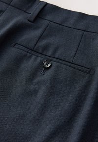 Tessuto di pantaloni eleganti blu navy scuro in primo piano che mostra una tasca posteriore con bottone nero e un motivo tessuto sottile.