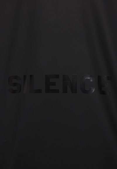 Tissu noir avec le mot "SILENCE" imprimé en lettres noires brillantes et en gras. La texture est lisse, créant un subtil contraste avec l'arrière-plan mat.