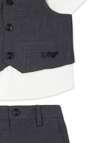 Gilet a scacchi grigi sovrapposto a una camicia bianca, con bottoni e tasca. Inclusi pantaloni a scacchi grigi abbinati. Dettaglio logo EA sul gilet.