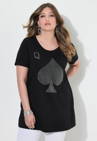 Camiseta negra con un gran diseño de trébol adornado con rhinestones y una pequeña "Q" en la parte superior izquierda, con escote redondo y mangas cortas.