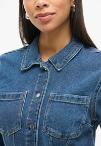 Denim jakna v svetloblui barvi, z ovratnikom, dvema sprednjima žepoma in srebrnim gumbom za zapiranje, okrašena z kontrastnimi šivi.