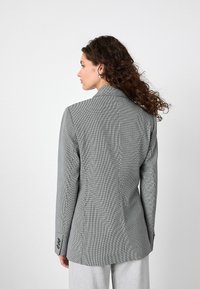 Grijs houndstooth-gepatroneerd blazer met een getailleerde pasvorm, aangeknipte revers en knoopmanchet. Gladde textuur en gestructureerde vorm.