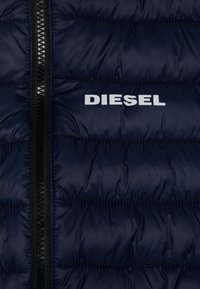 Mörkblå pufferjacka med horisontell sömnad, svart dragkedja och vit "DIESEL"-textlogotyp på bröstet. Slät, glänsande yta.