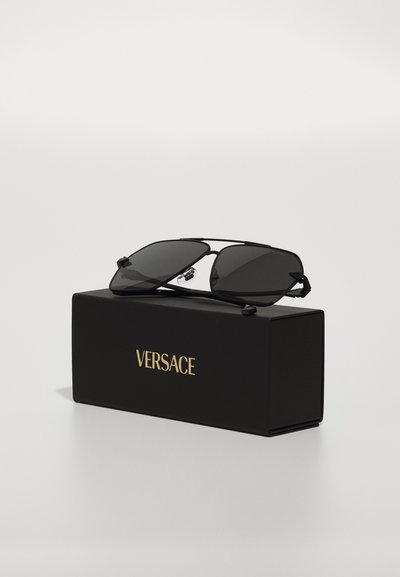 Lunettes de soleil rectangulaires noires avec des verres gris, dotées d'une monture en métal. Emballées dans une boîte noire avec "VERSACE" en lettres dorées.
