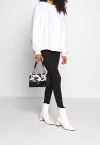 Valkoinen ylipitkä huppari, jossa on "MSG" -logo, mustat revityt skinny-farkut, valkoiset nilkkurit ja musta-valkoinen lehmäkuvioinen käsilaukku.