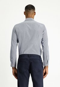 Camicetta button-up di colore azzurro chiaro con piccoli pois blu navy, dotata di maniche lunghe e colletto strutturato, abbinata a pantaloni elasticizzati blu scuro.