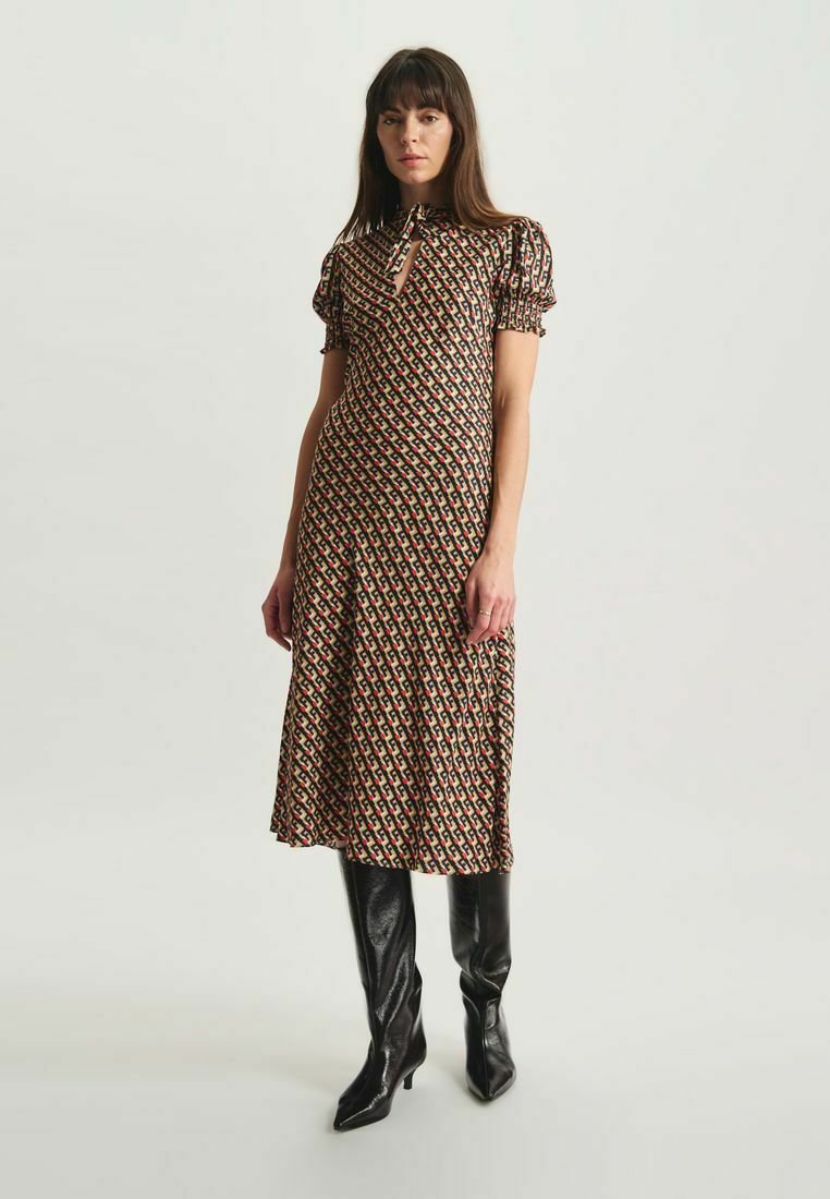 Robe midi imprimée avec des manches bouffantes, un col en cœur, et un motif géométrique dans des tons sombres. Associée à des bottes noires brillantes jusqu'aux genoux.