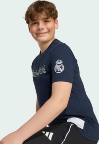 Námornícka modrá tričko s krátkymi rukávmi obsahuje vyšívané logo "Real Madrid" a klubový emblém na ľavom rukáve. Mäkká bavlnená textúra.