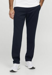 Pantalons de survêtement bleu marine en tissu doux, pr�ésentant un design à jambe droite et des poches latérales. Associés à des chaussures de sport blanches.