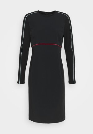 Sort langærmet kjole med rund hals. Har en rød vandret stribe ved taljen og kontrasterende blå lodrette striber på ærmerne.