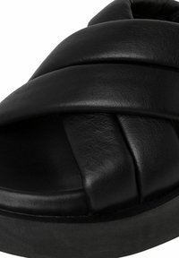 Sandale à glissière en cuir noir avec des sangles entrecroisées, forme arrondie, semelle rembourrée et semelle en caoutchouc épais. Texture lisse avec des accents minimaux.