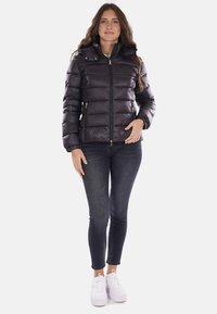 Giacca imbottita nera con chiusura a zip, polsini a coste e colletto alto. Presenta un design trapuntato e due tasche laterali.