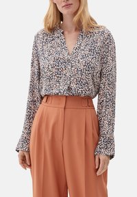 Kwiecista bluzka z długimi rękawami w kolorach granatowym, różowym i białym; posiada dekolt w kształcie litery V i luźny krój. Połączona z pomarańczowymi spodniami o wysokim stanie i szerokich nogawkach.