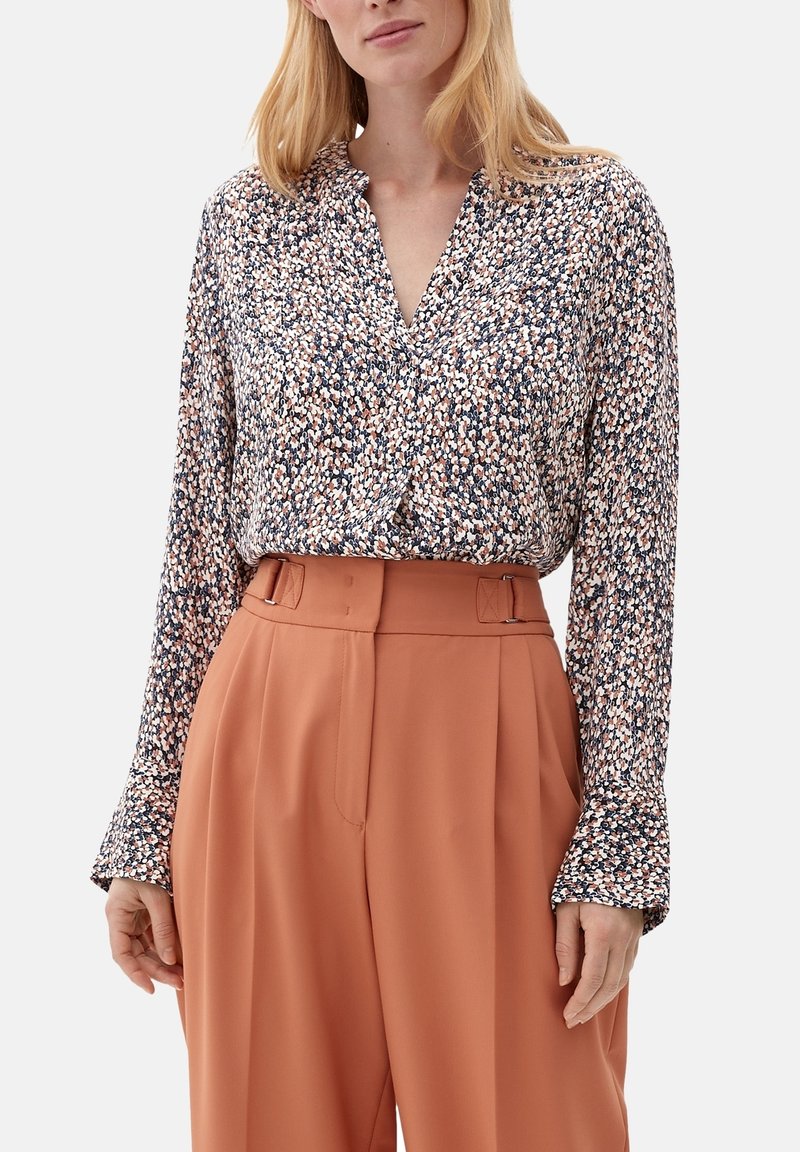 Kwiecista bluzka z długimi rękawami w kolorach granatowym, różowym i białym; posiada dekolt w kształcie litery V i luźny krój. Połączona z pomarańczowymi spodniami o wysokim stanie i szerokich nogawkach.