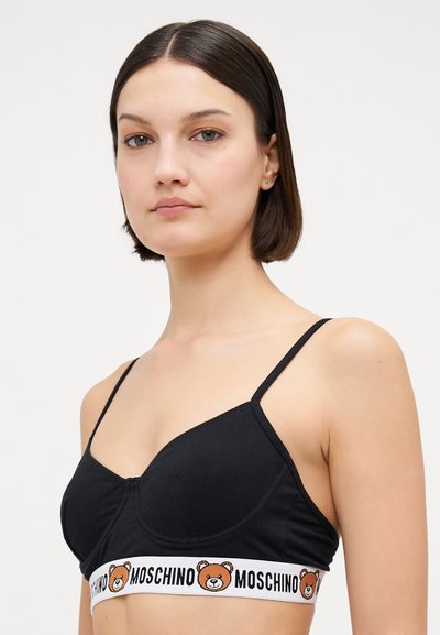 Crni pamučni bralette s tankim podesivim trakama, koji se ističe bijelim pojasom s ilustracijom medvjeda i natpisom "MOSCHINO."