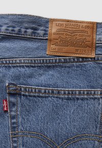 Tasca posteriore di jeans in denim blu con etichetta rossa Levi's e patch in pelle marrone Levi Strauss & Co. che mostra la taglia W32 L32.