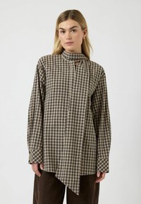 Brun og beige ternet skjorte med lange ærmer, høj krave, knapper foran og asymmetrisk kant. Fremstillet af et struktureret stof.