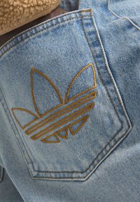 Jeanstyg i ljusblått med en strukturerad yta, med en gyllene broderad logotyp i en triangulär design på bakfickan.