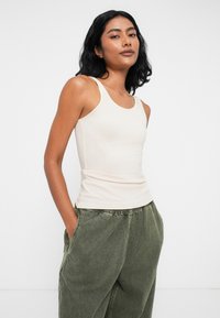 Gaiši beigtu topiņu ar šaurām siksnām, pieguļošs dizains, izgatavots no mīksta auduma. Apvienots ar brīviem olīvu zaļas biksēm, kurām ir sānu kabatas.