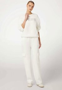 Sweat-shirt blanc avec "DRESS" en argent sur le devant, associé à un pantalon cargo blanc assorti avec des poches latérales et une coupe décontractée.