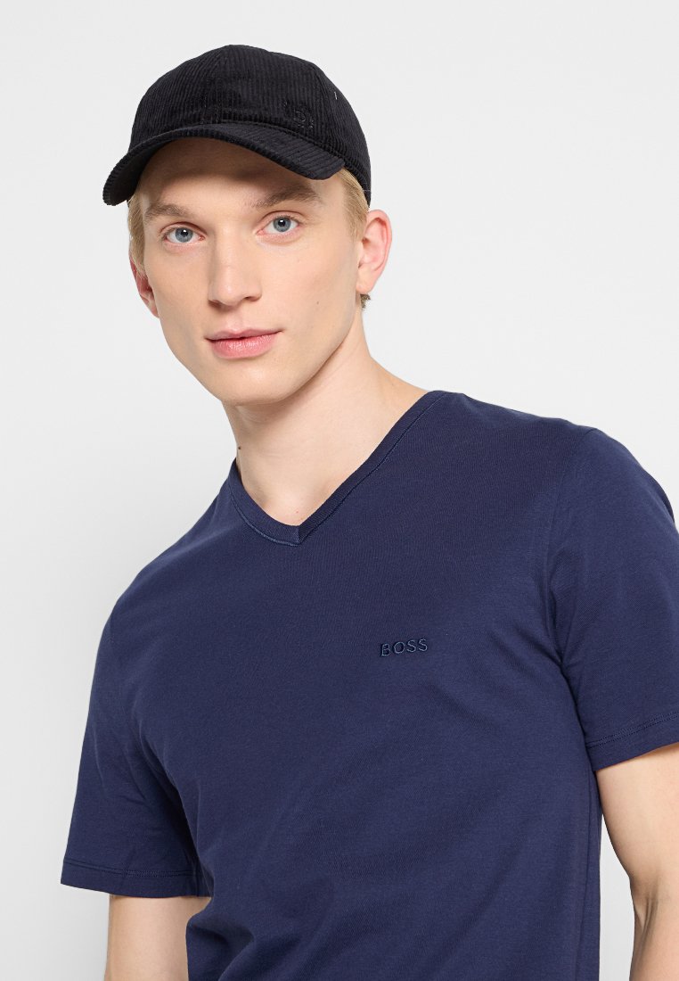 Gorra de pana negra, camiseta de cuello en V azul marino con el logotipo bordado de "BOSS". La camiseta tiene un corte ajustado, mangas cortas y una textura suave.