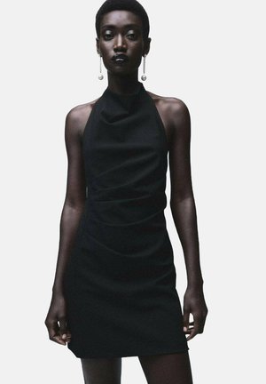 Vestido mini negro de tirantes con un tejido suave, con detalles fruncidos en el costado y una silueta ajustada. Presenta pendientes de perlas.