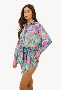 Set van lange mouwen shirt en shorts in een levendig roze, groen en paarse tropische bladerenpatroon. Bevat een knoopsluiting aan de voorkant en een strikdetail in de taille.