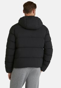 Giacca a vento nera con cappuccio, caratterizzata da un design trapuntato e una vestibilità morbida. Texture soffice con sezioni cucite visibili.