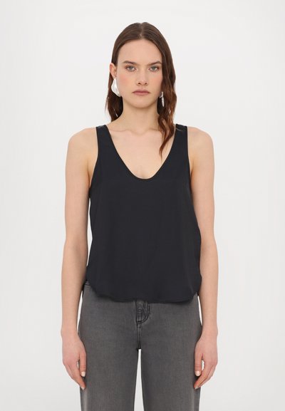 Top noir sans manches avec un décolleté en V profond, en tissu doux, coupe décontractée et ourlet arrondi. Assorti avec un jean gris. Sans motifs ni éléments en métal.