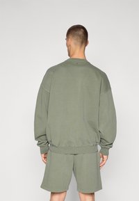 Túlméretezett, hosszú ujjú pulóver és hozzáillő sort hazai olíva zöld pamutból. Ribbed mandzsettákkal és derekú résszel rendelkezik, laza illeszkedéssel.