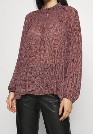 Fließende Bluse mit langen Ärmeln, die ein strukturiertes, gewelltes Muster in Rot- und Violetttönen aufweist. Mit rüschigem Ausschnitt und Schlüssellochdetail.