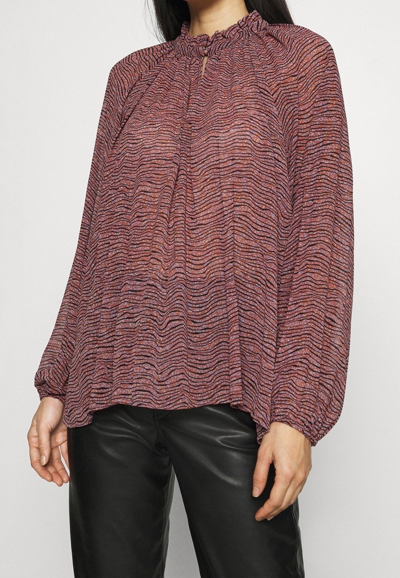 Fließende Bluse mit langen Ärmeln, die ein strukturiertes, gewelltes Muster in Rot- und Violetttönen aufweist. Mit rüschigem Ausschnitt und Schlüssellochdetail.