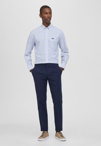 Camicia a righe button-up di colore azzurro chiaro e bianco, abbinata a pantaloni blu navy e sneaker beige. Tra i dettagli notevoli c'è una tasca sul petto.