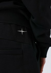 Zwarte joggingbroek met een geribbelde tailleband en een kleine witte sterborduring op de achterzak. Zachte, gestructureerde stof.
