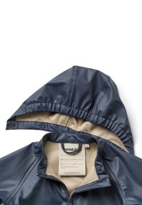Chaqueta impermeable de color marino con capucha forrada, cremallera frontal y cierres a presión. El interior incluye una etiqueta con la marca y detalles de cuidado.