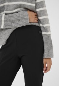 Gray striped knit sweater with ribbed sleeves and black fitted trousers featuring two black button accents on the waistband.