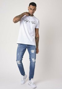 White short-sleeve t-shirt with "Project x Paris" printed in black, paired with blue ripped skinny jeans and white sneakers.