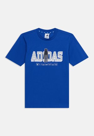 Niebieski t-shirt z krótkim rękawem z pikselowanym białym tekstem "ADIDAS" i czarną postacią Endermana z Minecraft stojącą na środku tekstu.
