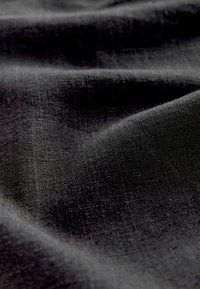 Černá látka s měkkým, texturovaným povrchem a jemným leskem, vykazující mírné záhyby a sklady v tkaném vzoru.