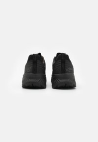 Zwarte hardloopschoenen met een mesh bovenkant, een gevoerde middenzool en diepe loopvlakken voor grip. Korte trek lussen aan de hiel voor gemakkelijk aan- en uittrekken.