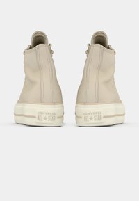 Beige Converse høye sneakers med en glatt lærfinish, med tonalt søm og en hvit gummisåle med preget logo på hælen.