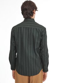Camisa de manga larga verde oscuro con rayas verticales, puños abotonados y dobladillo curvado. Tejido suave y diseño estructurado en los hombros.