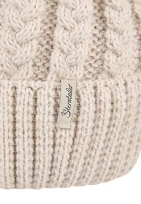 Beige knitted wool hat with cable-knit pattern and a small fabric tag reading "Sterntaler" sewn onto the ribbed brim.
