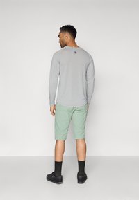 Siva majica dugih rukava s okruglim izrezom, uparena s mint zelenim šortsevima do koljena. Crne čarape i cipele upotpunjuju odijelo.