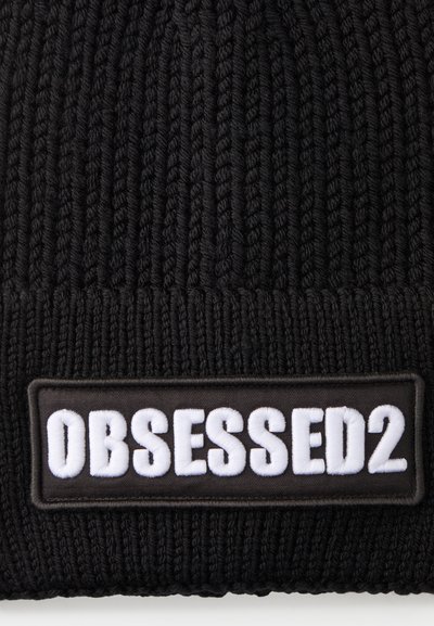 Sort strikket beanie med ribbet tekstur. Har et rektangulært sort mærke med "OBSESSED2" i hvid broderi.