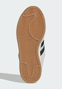 Podrážka topánky s textúrovaným, vlnitým gumovým vzorom v hnedej farbe, lemovaná krémovým zvrškom, s tromi čiernymi pruhmi ako dizajnový detail.
