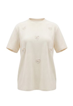 Crèmekleurig T-shirt met korte mouwen en zes kleine hartapplicaties met kanten rand gelijkmatig verdeeld aan de voorkant. Geen zichtbare achtergrond of model.
